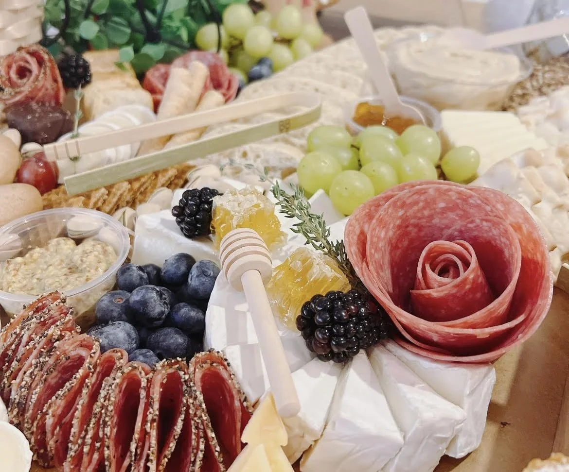 Charcuterie board with grapes, blueberries, slices of salami arranged like a rose, cheeses, honey, and other appetizers.