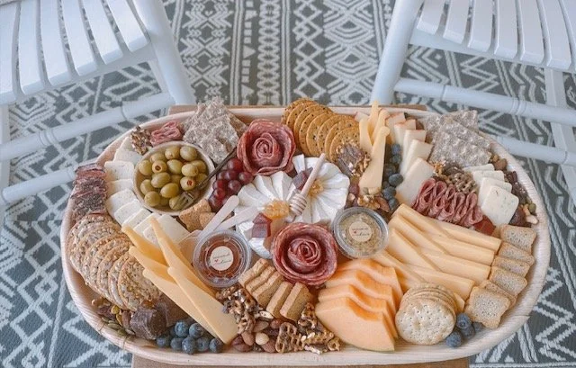 A large cheese and charcuterie platter with assorted cheeses, cured meats, crackers, olives, grapes, and nuts, arranged on a white oval tray.