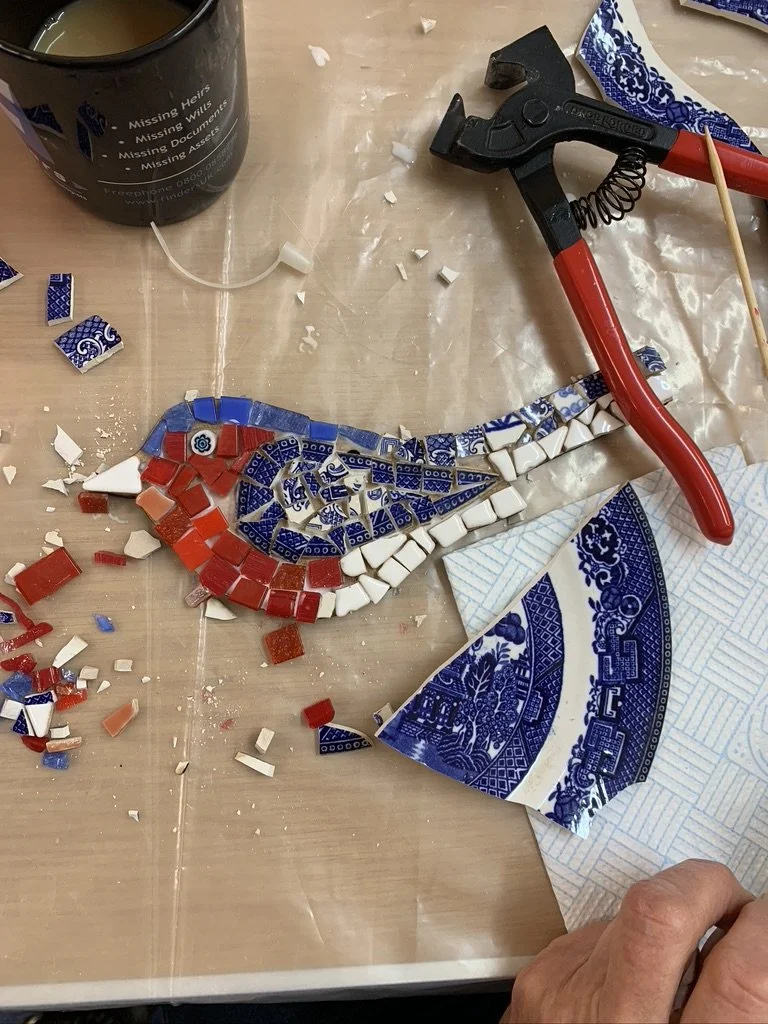 Vintage china being cut and arranged into a mosaic bird during a CreatingART adult mosaic workshop in Wales.