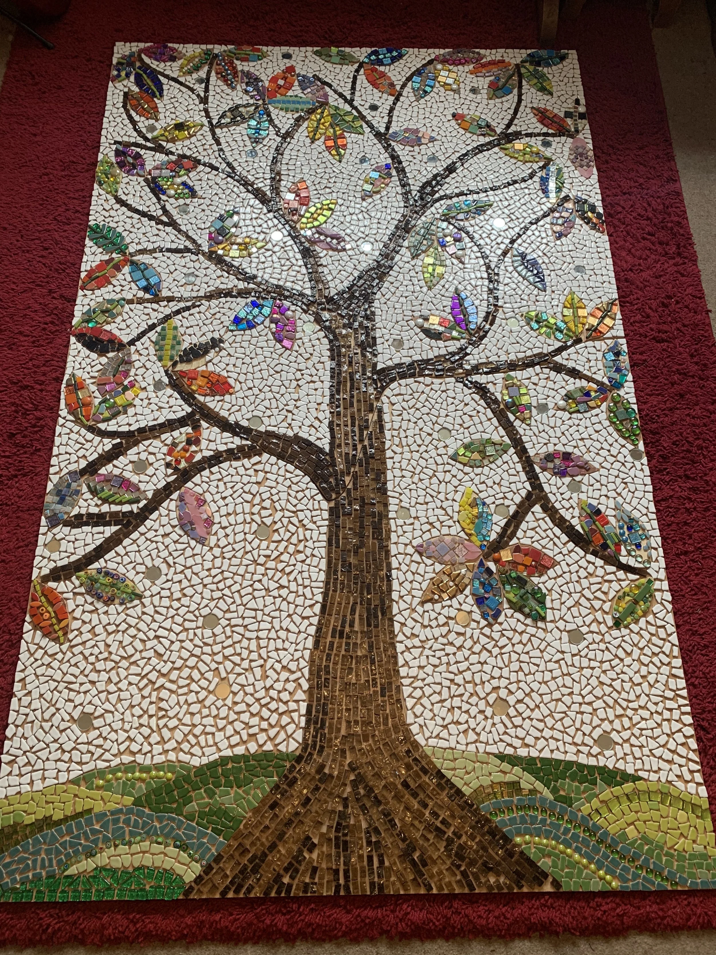 Mosaic artwork featuring a large tree with colorful leaves on a white background with a red border.