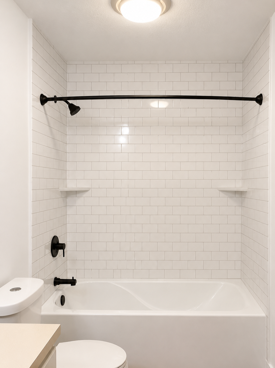 Bathroom with white acrylic subway tile shower area, black fixtures, a white bathtub, a toilet, a beige countertop, and a ceiling light fixture.  Easy to clean acrylic shower and deep soaker tub installed in just one day in Urbandale, Iowa.