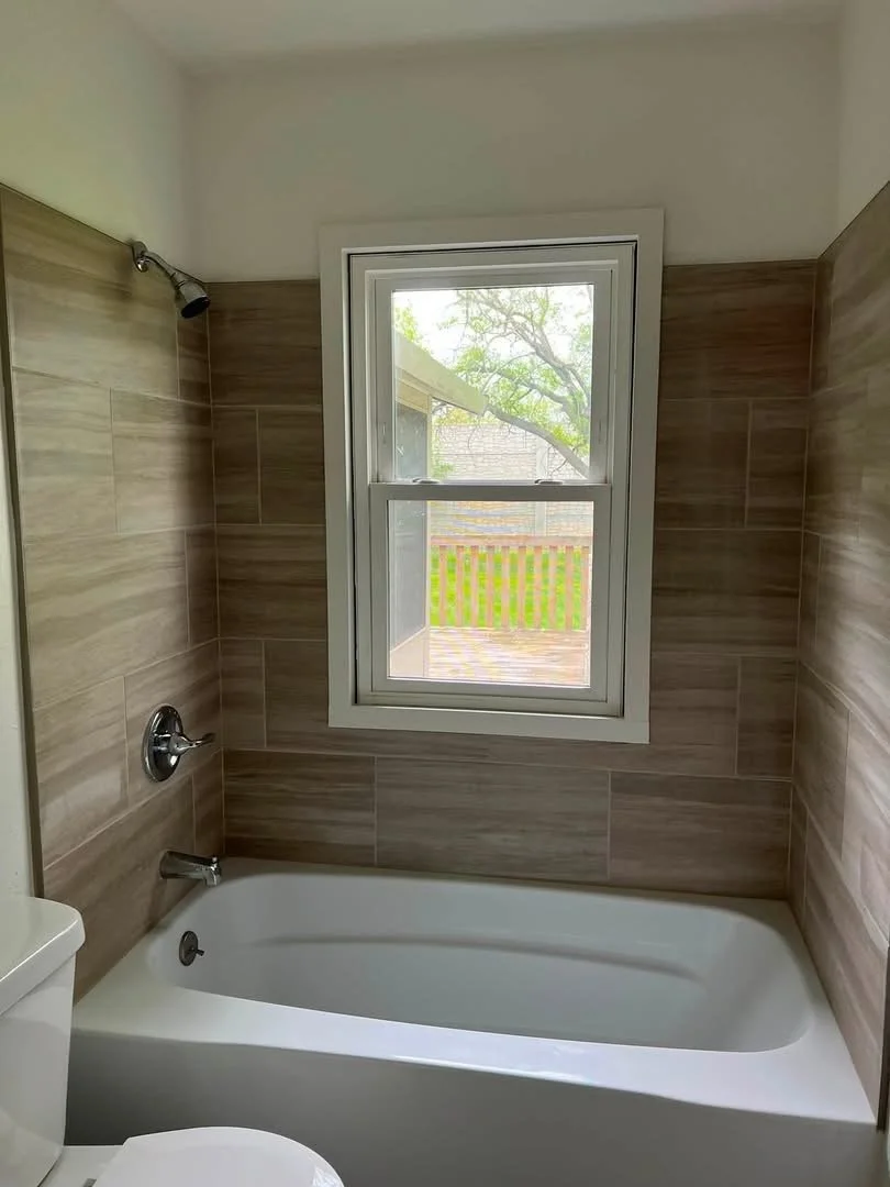 Bathroom with bathtub, brown tiled walls, and a window showing outdoor greenery.