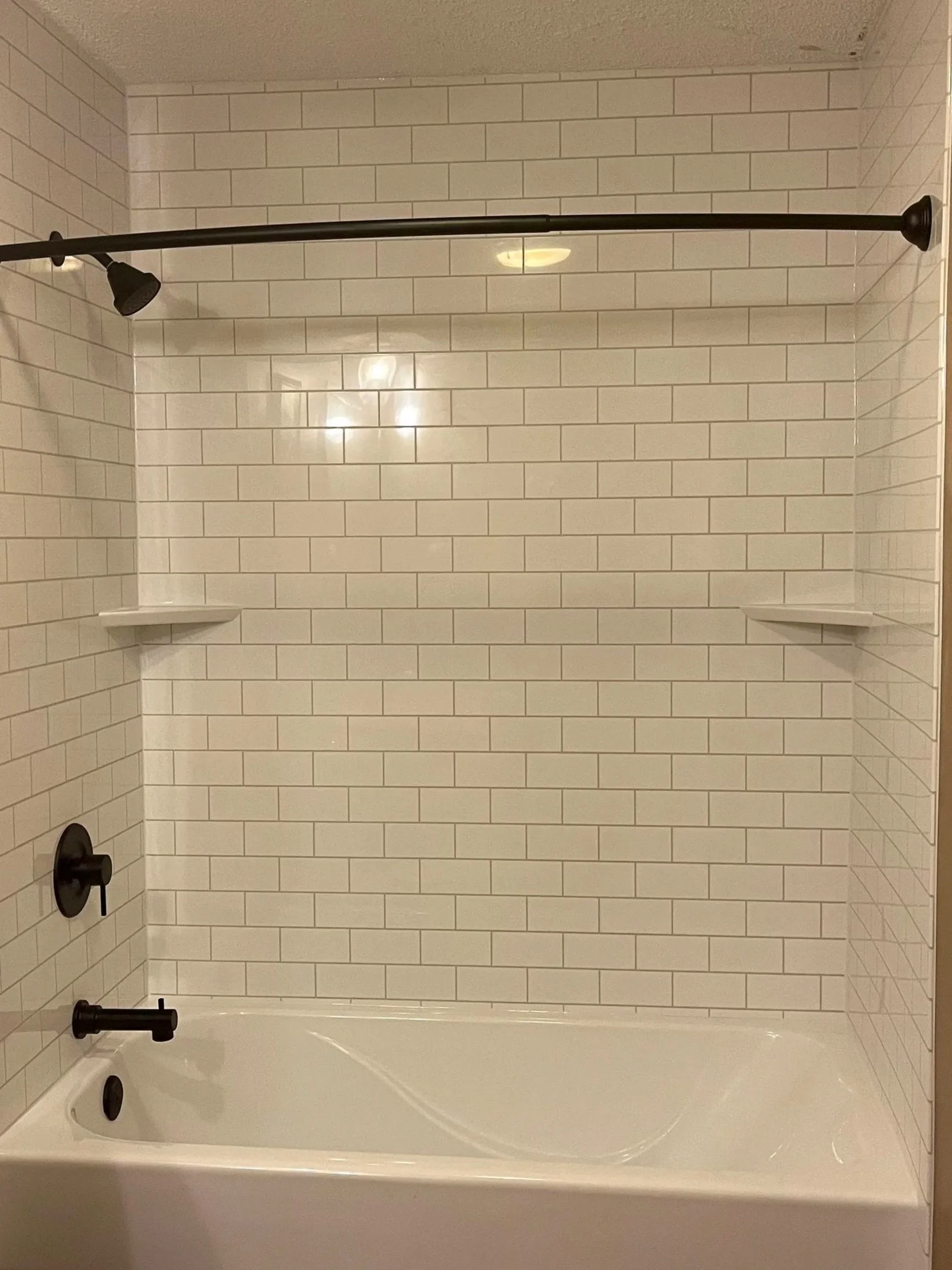 Bathroom shower with white subway tile walls, black shower fixtures, and a white bathtub.  Easy to clean acrylic shower installed in one day in Urbandale, Iowa.