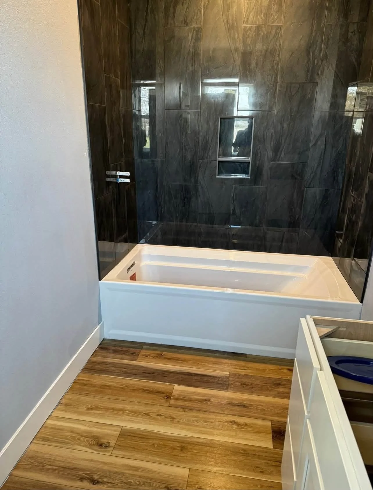 Bathroom with a bathtub, dark gray marble wall tiles, and a small built-in niche.