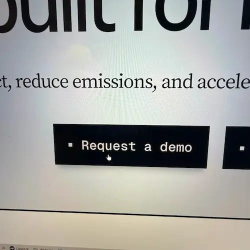 A computer screen displaying a webpage with a black button labeled 'Request a demo' and some text about reducing emissions and accelerating.