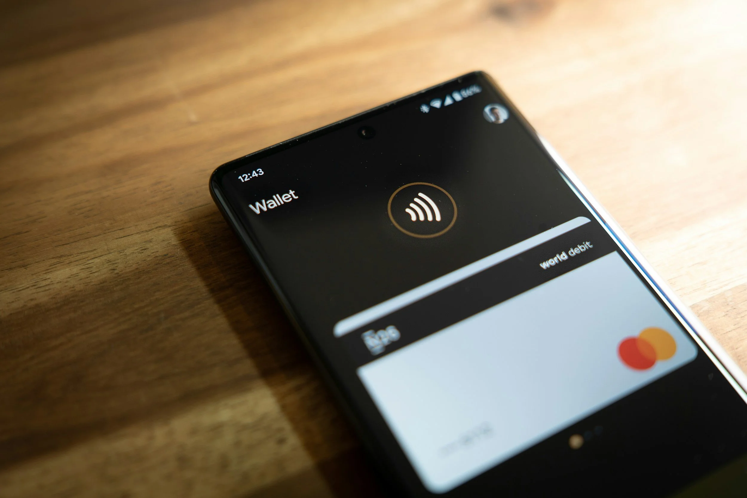 Close-up of a smartphone displaying a digital wallet app with contactless payment icon on the screen, placed on a wooden surface.
