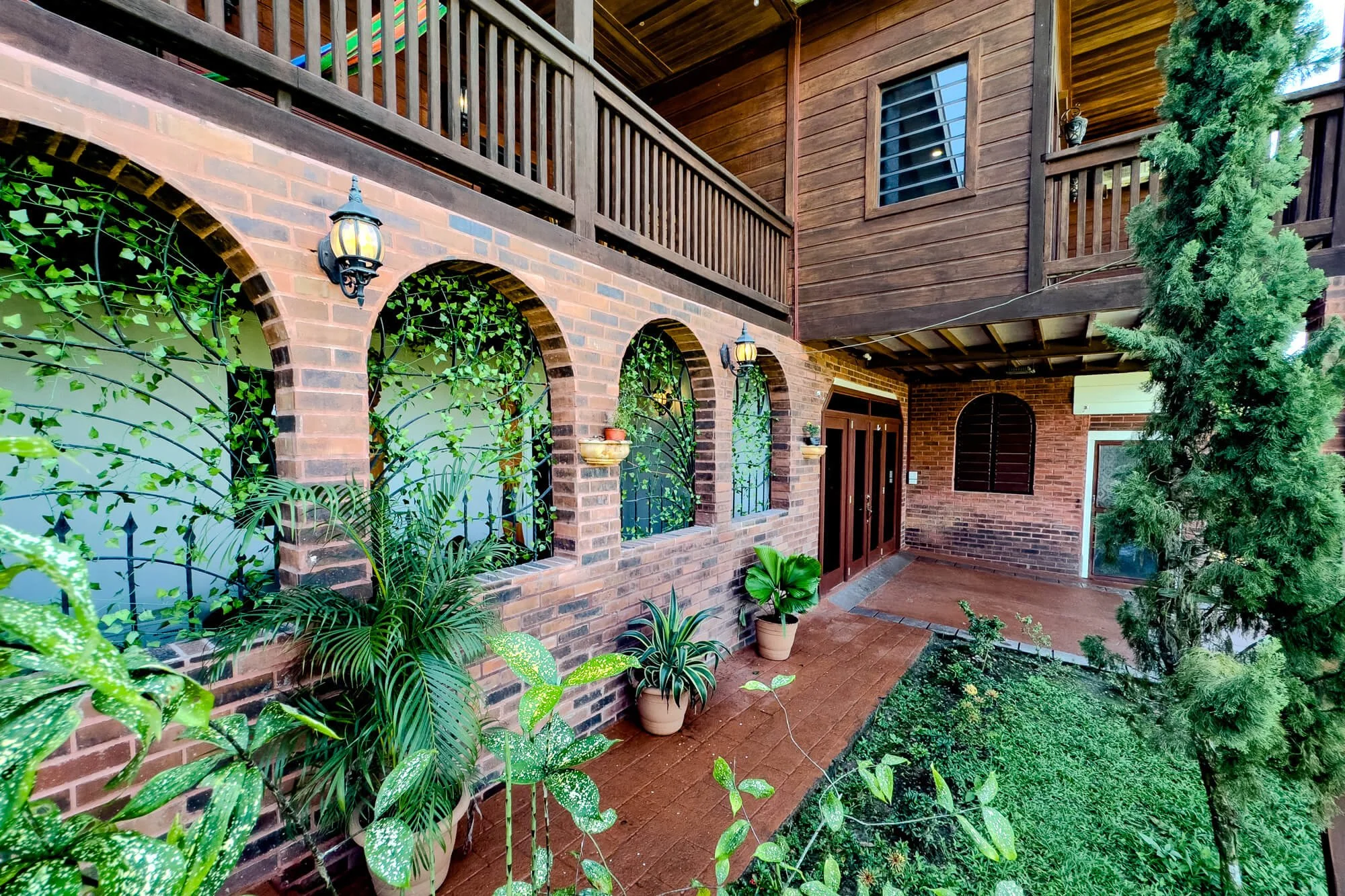 Exterior of Cayo Mountain View Estate in Santa Elena, Belize, featuring the brick lower level, timber upper level, wraparound verandah and tropical landscaping.