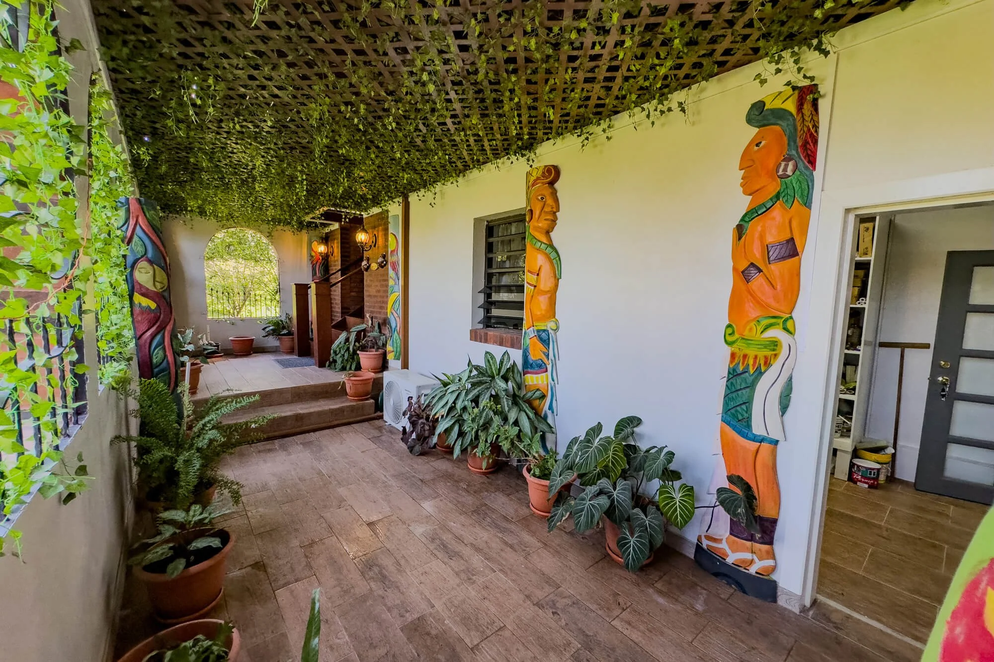 Covered patio at Cayo Mountain View Estate featuring tropical plants, colorful Belizean artwork and access to the surrounding outdoor living areas.