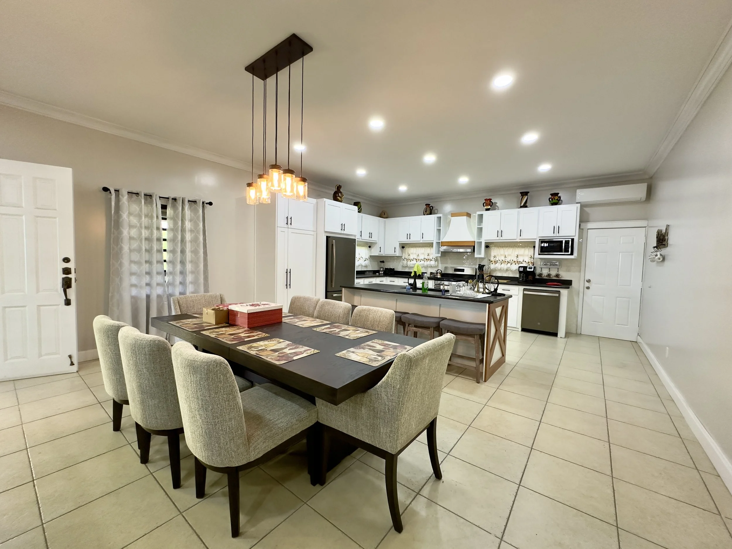 Dining area adjoining the bright modern kitchen at Cayo Mountain View Estate, with tiled floors, white cabinetry and generous interior space.