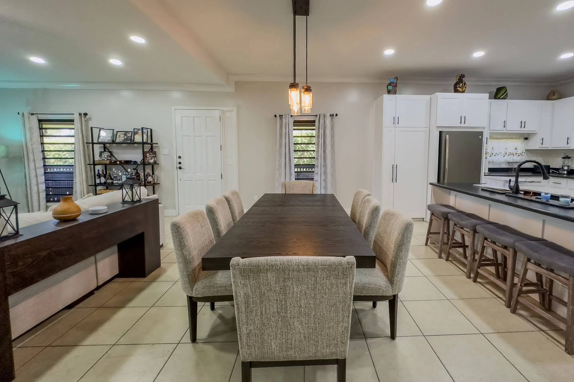 Dining area and adjoining modern kitchen at Cayo Mountain View Estate, featuring an island, bar seating, white cabinetry and spacious open-plan design.