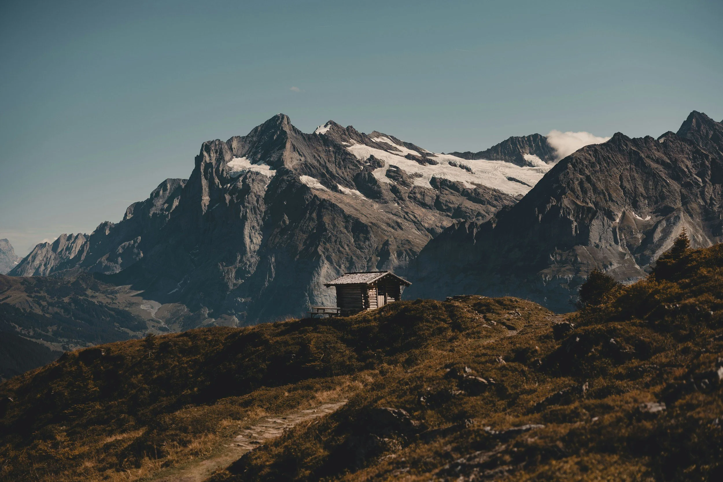 small cabin perched on an elevated position overlooking an intimidating and sublime mountain range towering in the distance