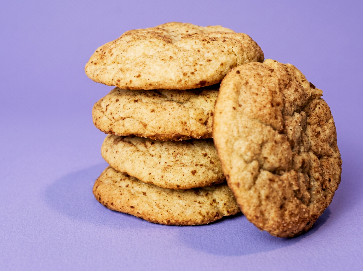 Four sinkerdoodle cookies stacked vertically with a fifth cookie leaning against the stack, on a purple background.