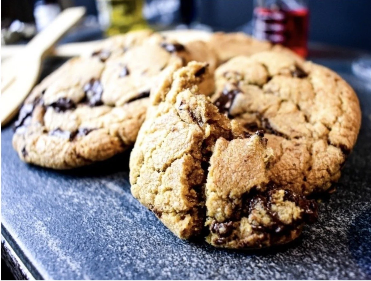 Close-up of cookies with chocolate chunks on a dark surface.