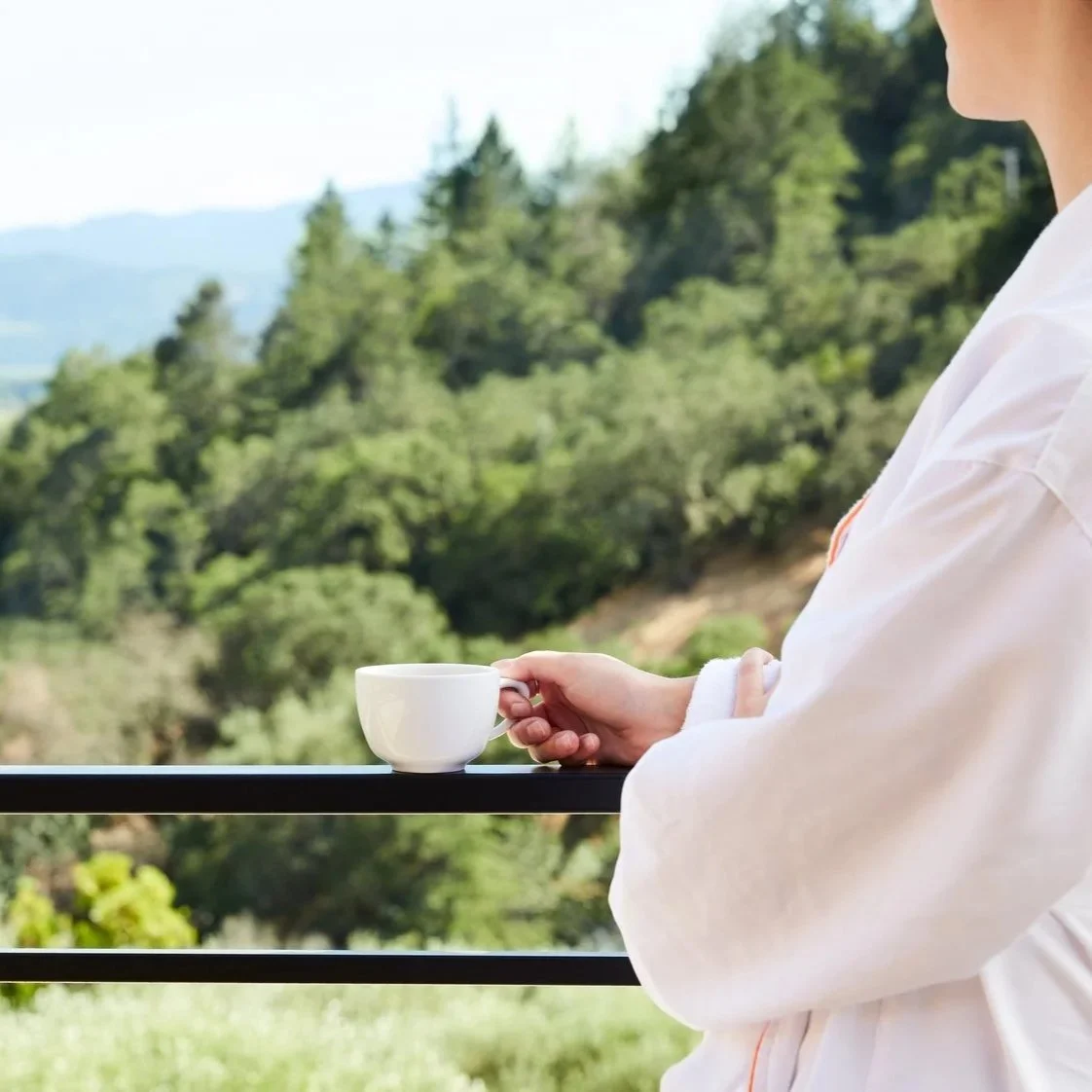 Woman in a robe enjoying coffee from a resort balcony