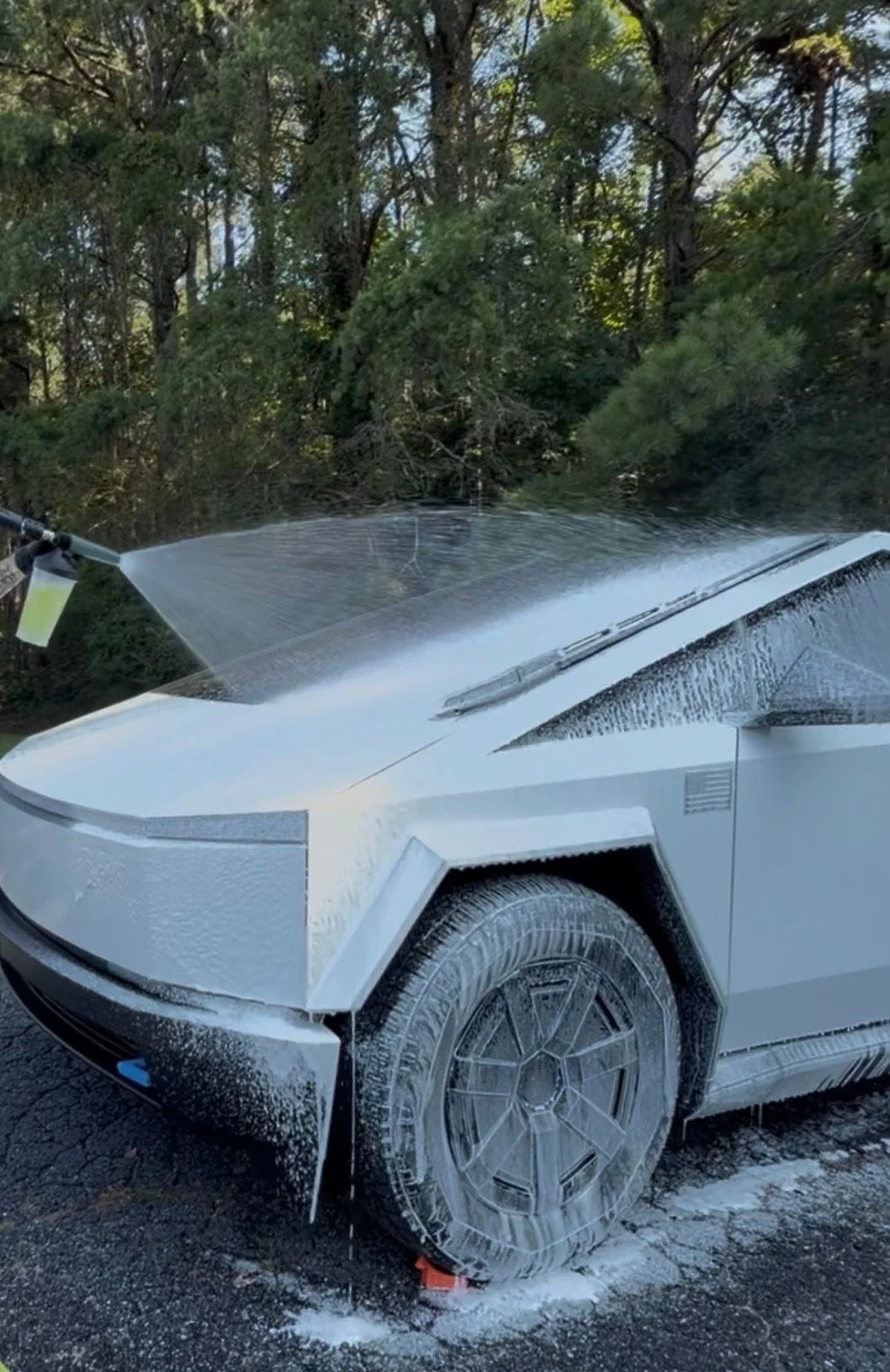 Foam wash on a white Cybertruck, with the front wheel and body covered in suds.
