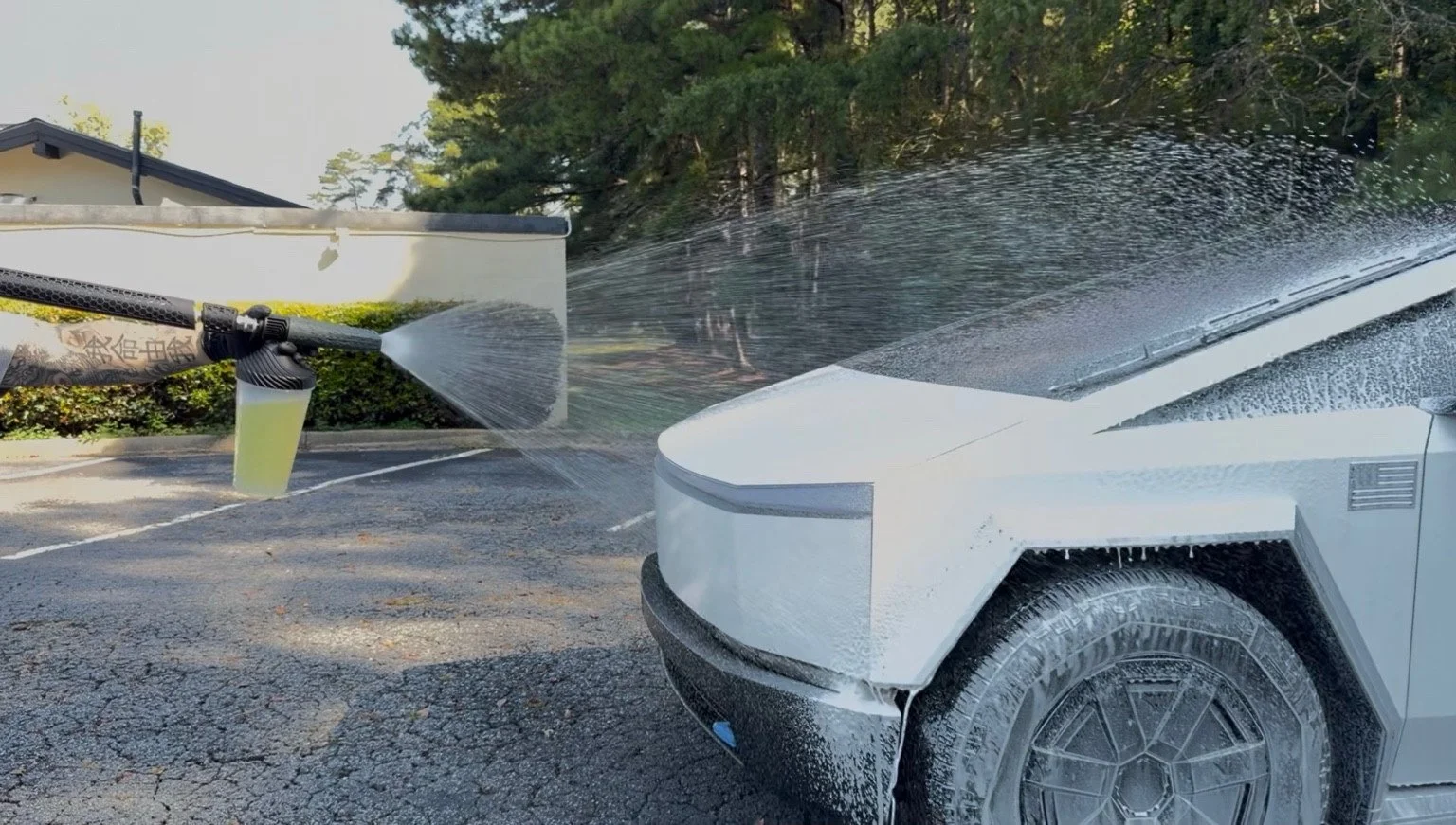 Foam cannon applying suds across the front of a white Cybertruck.