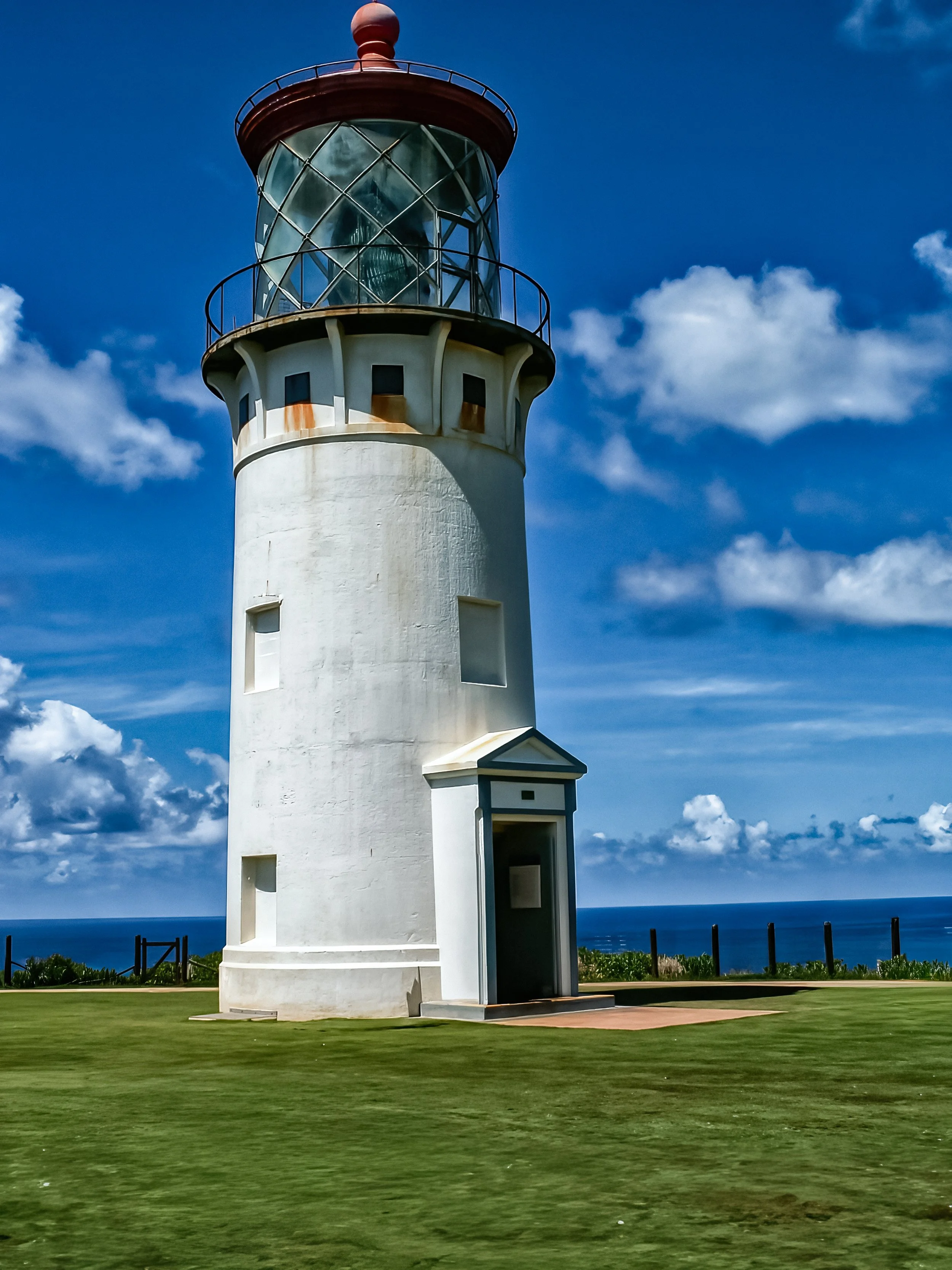 The Kilauea Lighthouse - A striking view of the historic Kilauea Lighthouse standing tall against a vivid blue Hawaiian sky, overlooking the Pacific Ocean.