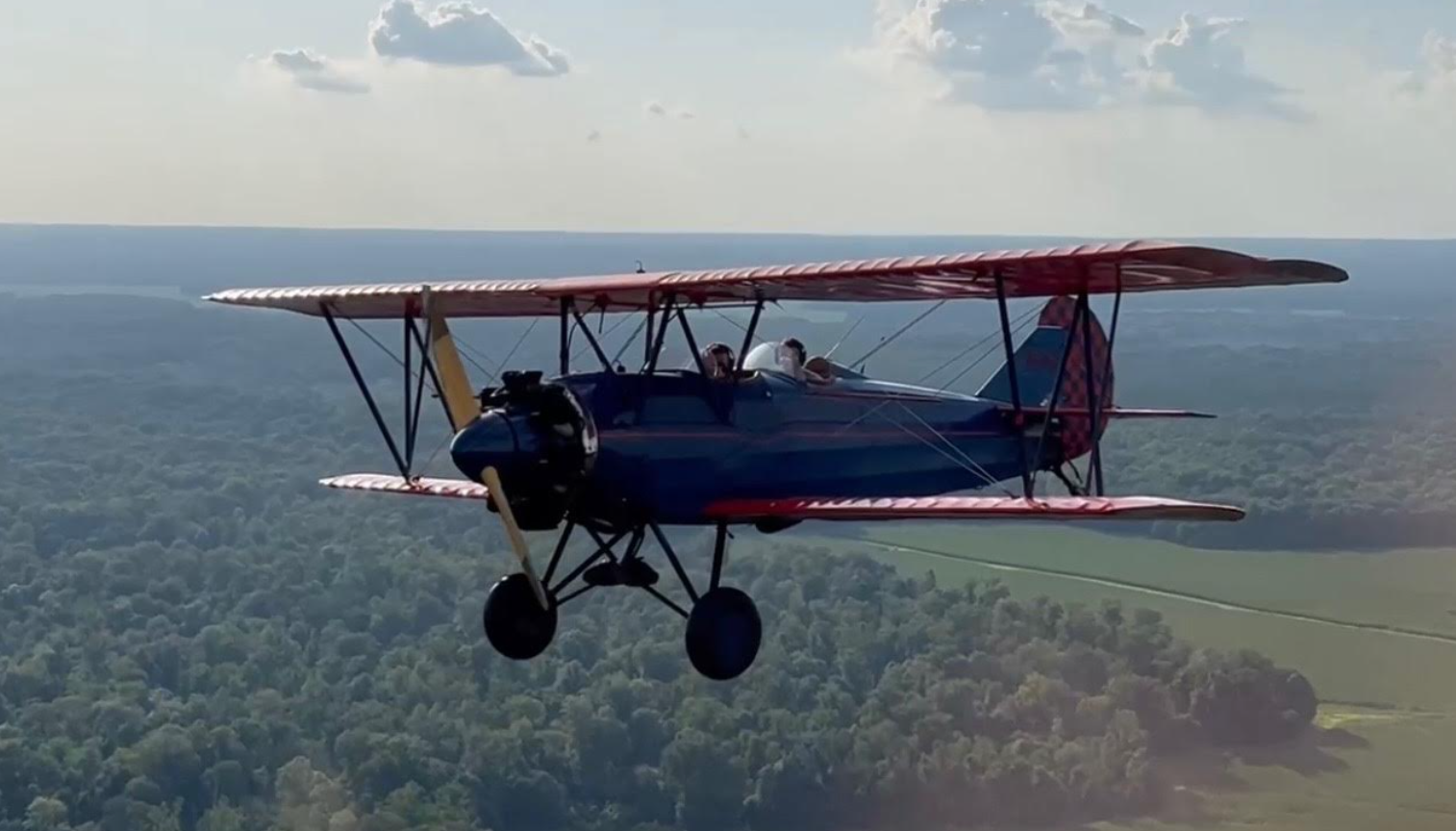 A biplane flying over a forested landscape during the daytime.