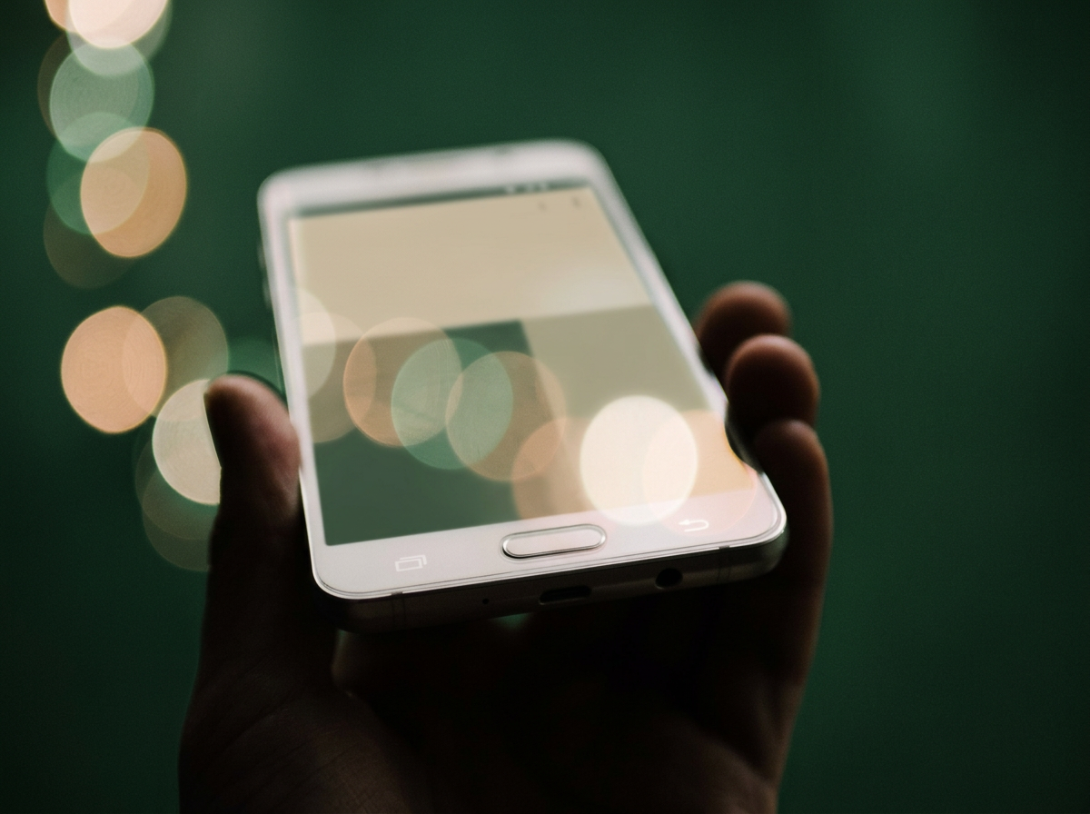 Hand holding a smartphone with a blurred background of circular lights.