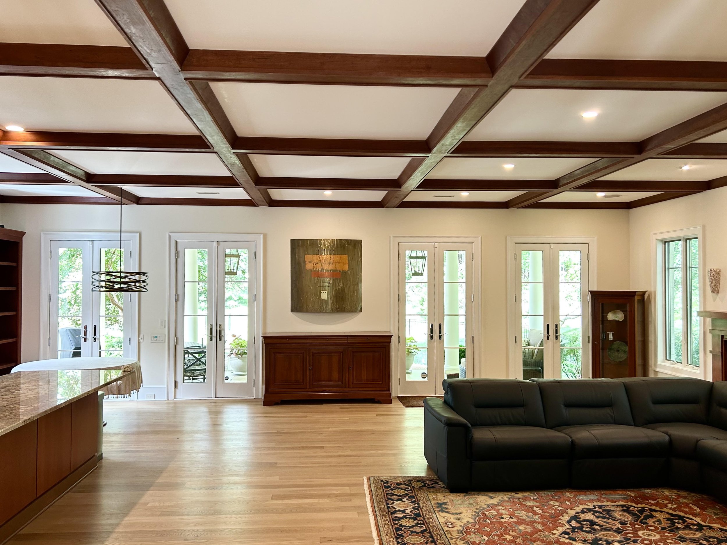 Living room interior with wood beams on ceiling, French doors, a black leather sofa, and a decorative rug on hardwood flooring.
