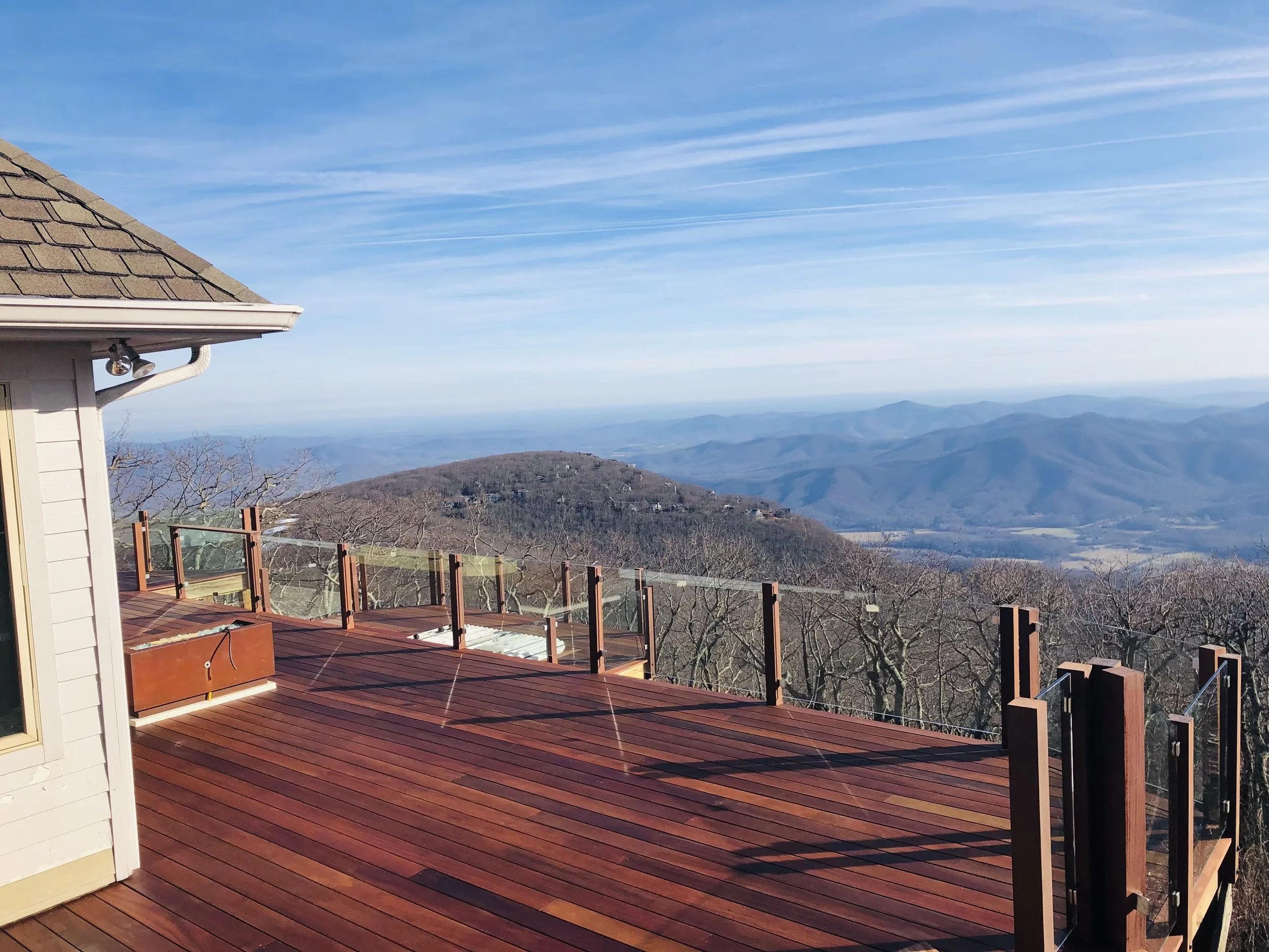 View of a wooden deck overlooking a mountainous landscape with clear blue sky and wispy clouds.