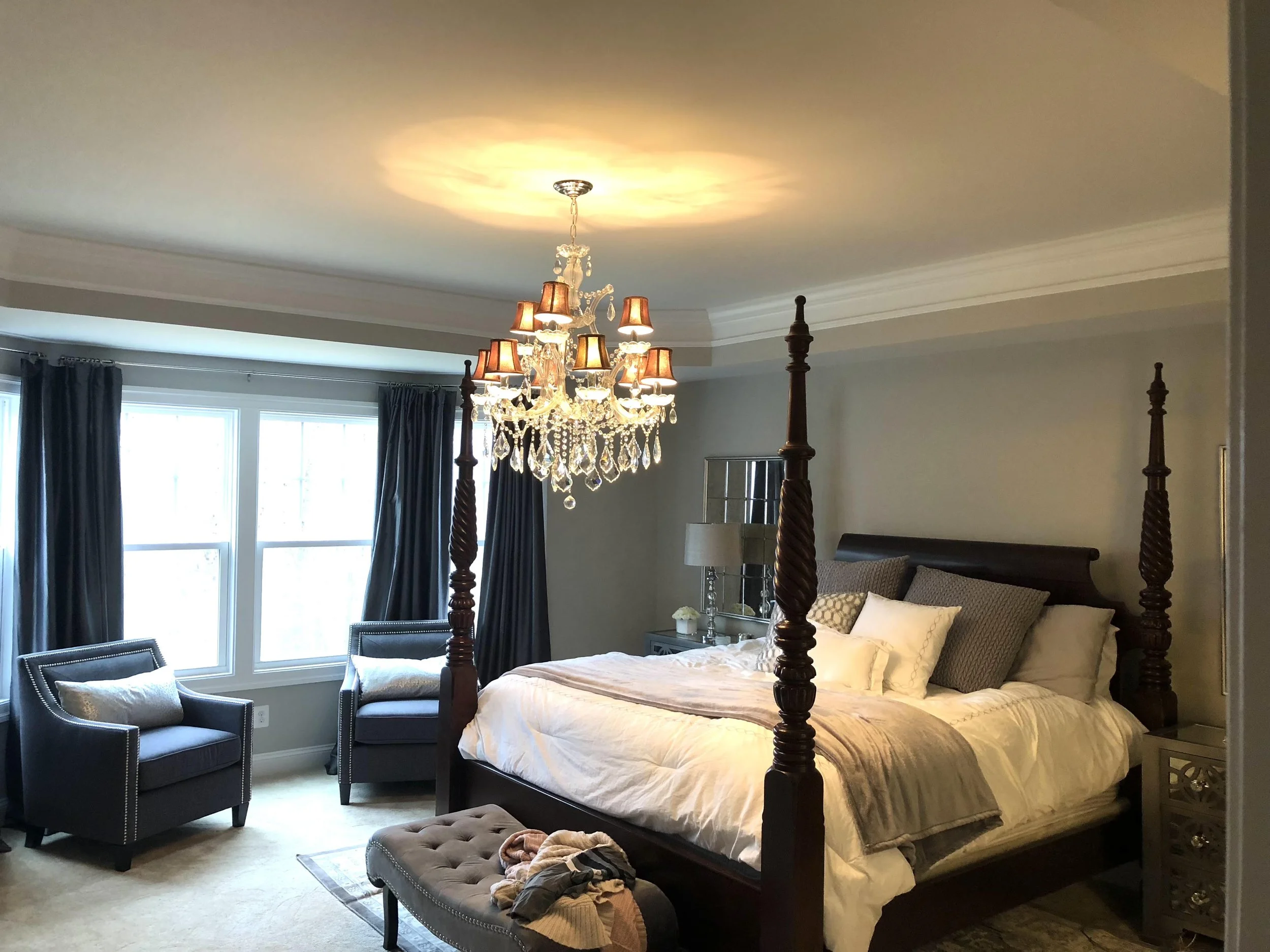 A bedroom with a four-poster bed, a chandelier, and large windows with dark curtains.