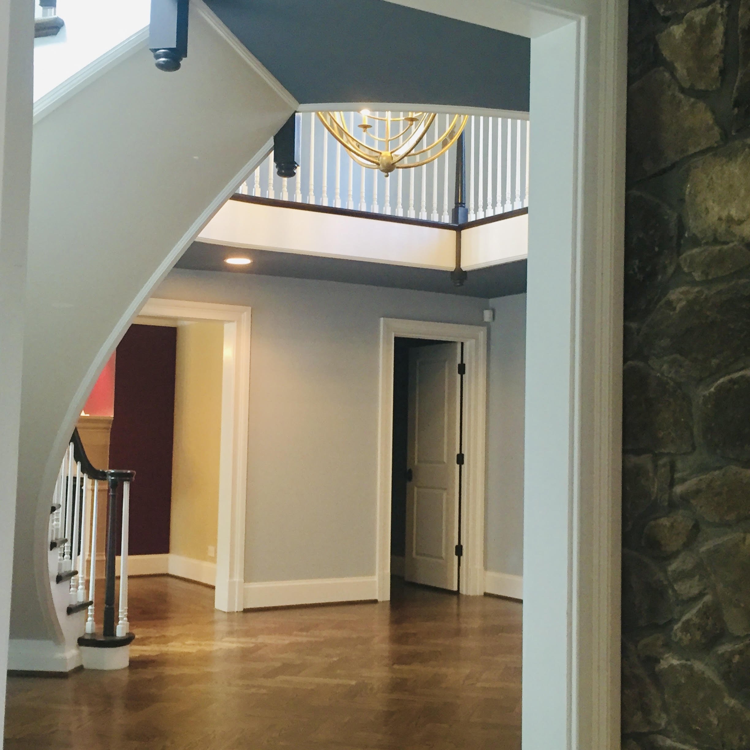 View of a staircase with a gold chandelier hanging from the ceiling, overlooking a wooden-floored living area with yellow and maroon walls, and a bedroom or hallway in the background.