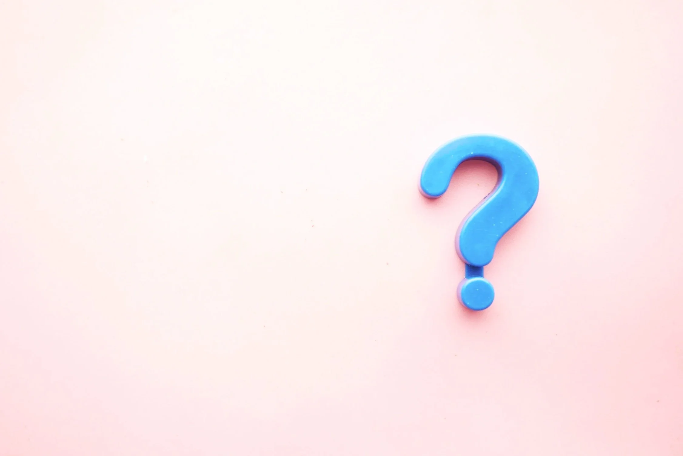 A blue question mark made of plastic on a light pink background.