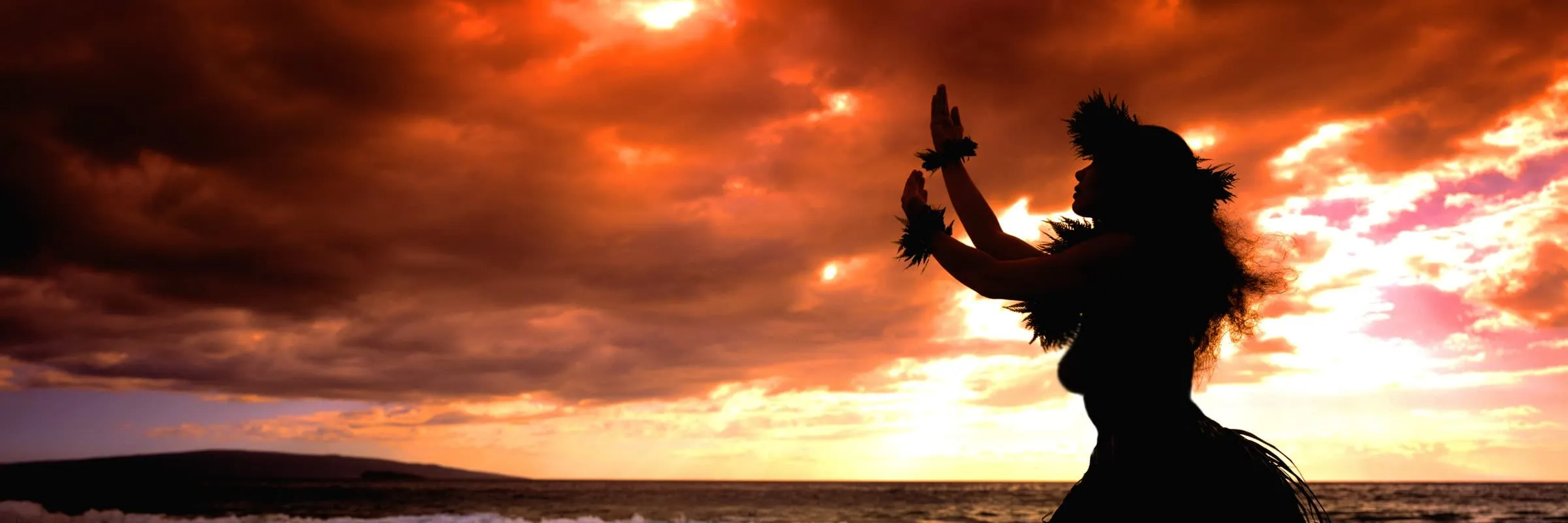Silhouette of a person dressed in traditional Polynesian attire, dancing against a colorful sunset over the ocean.