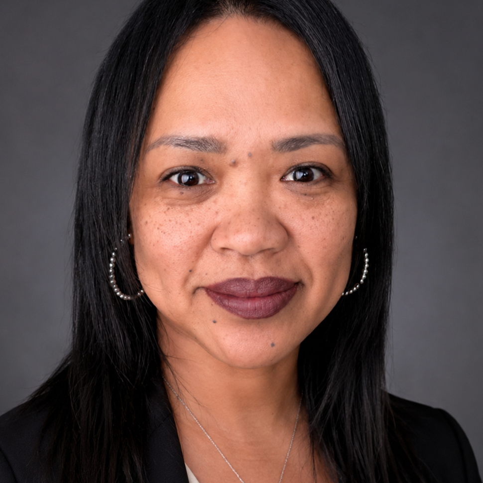 Portrait of a woman with black hair, hoop earrings, and wearing a black blazer against a gray background.