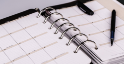 Open spiral-bound planner with blank calendar pages and a black pen on top