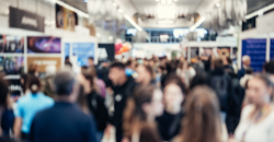 Crowded indoor event with many people, displayed screens, and booths.
