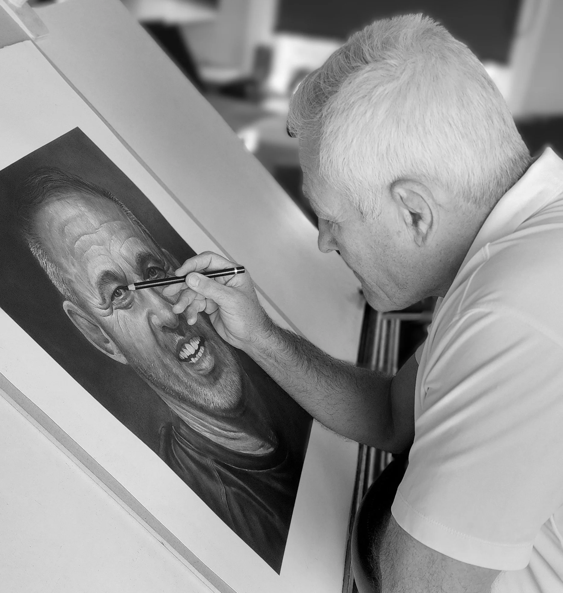 A man with short, light-colored hair is sitting on a white toilet and leaning forward, touching a framed RGB photograph of an elderly man with glasses and a big smile on a table.