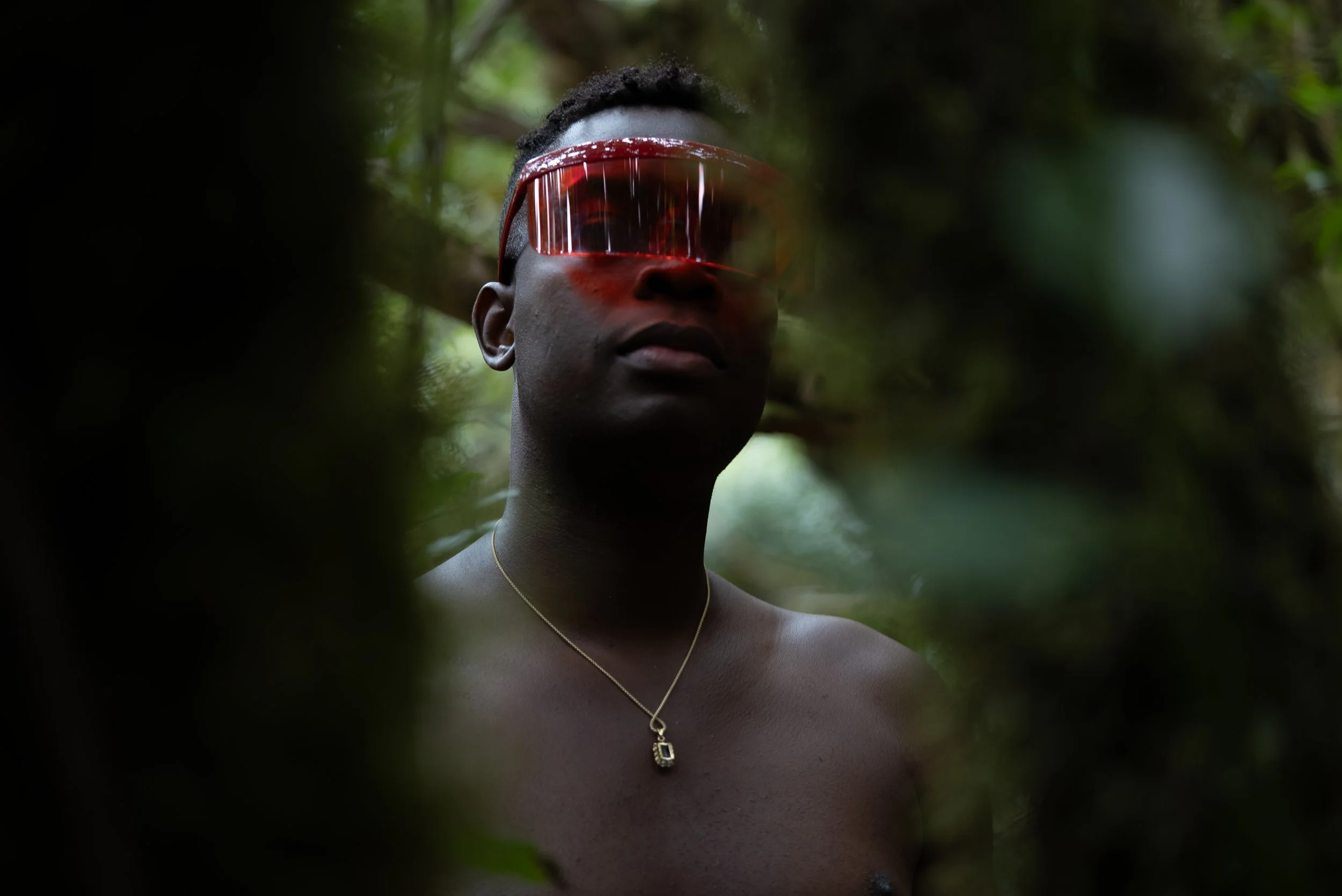 Portrait of a Black man wearing red glasses behind a tree in the middle of a forest