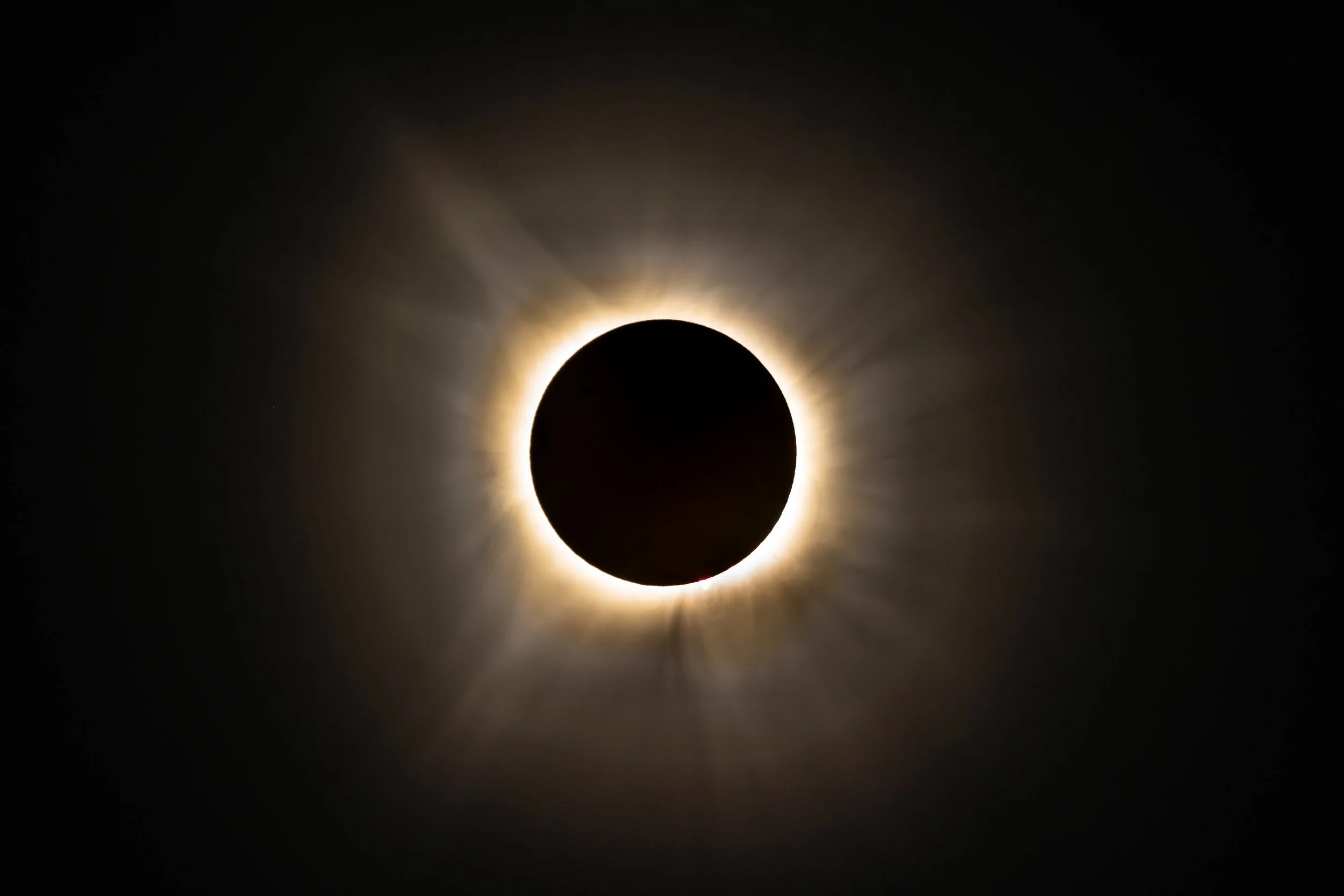 A solar eclipse with the moon covering the sun's center, creating a glowing halo and rays of light radiating outward.