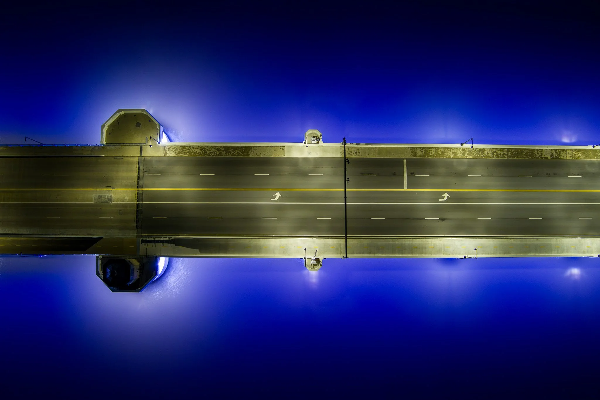 Nighttime view of an airport runway and terminal structure with bright lights and reflections on the water below.