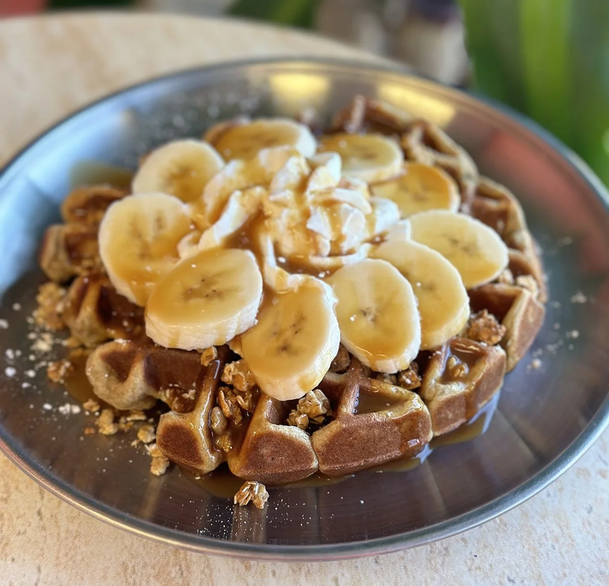 Protein Waffle topped with sliced bananas, caramel sauce, nuts, and whipped cream on a metal plate.