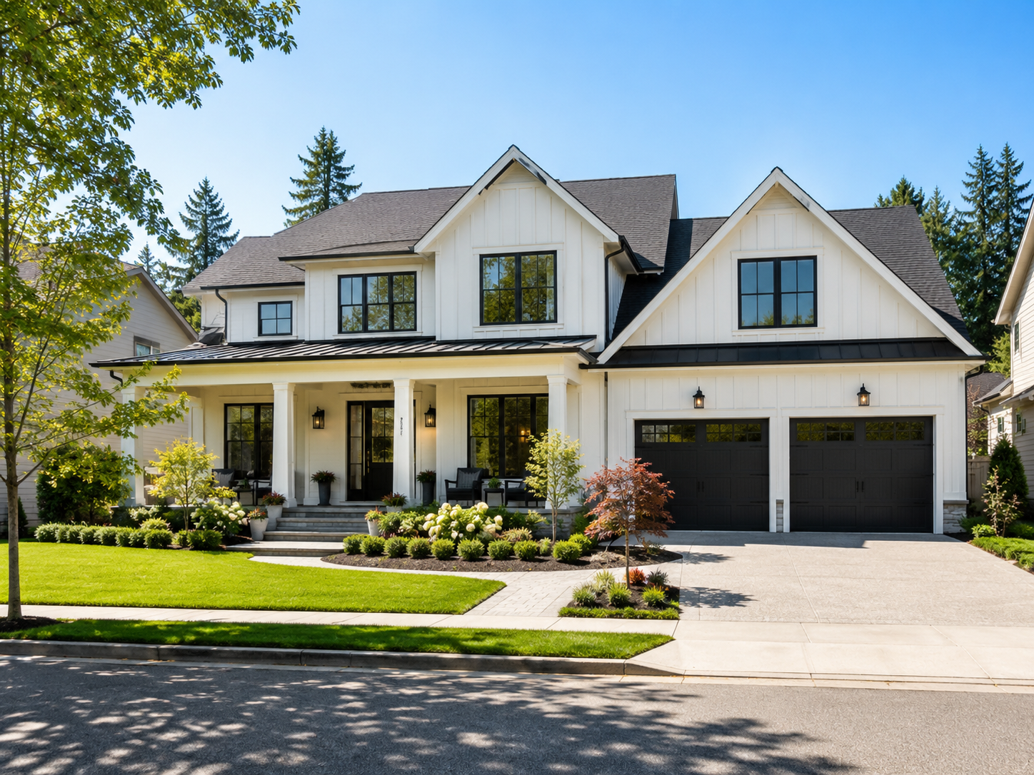 Front view of a modern two-story white house with black garage doors, large windows, a covered porch, and landscaped front yard with green grass, small trees, and shrubs, under a clear blue sky.