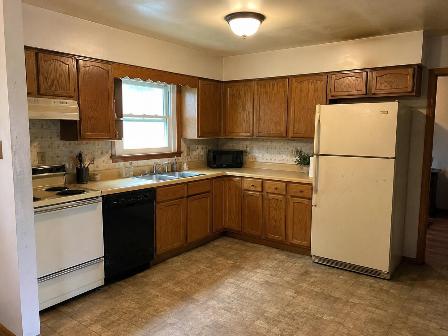 Kitchen with wooden cabinets, a window over the sink, a white refrigerator, a black dishwasher, stove, microwave, and small potted plant on the counter.