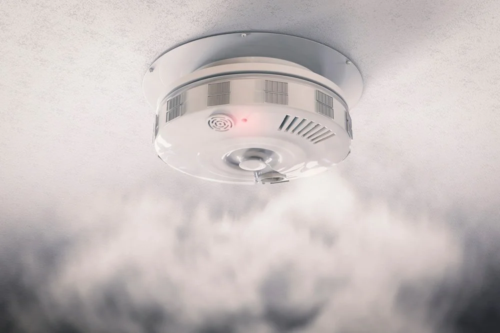 Fire alarm smoke detector emitting smoke or mist against a ceiling.