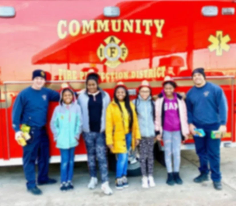 Group of people standing in front of a red fire department vehicle with 'COMMUNITY' and 'FIRE DEPARTMENT DISTRICT' written on it.