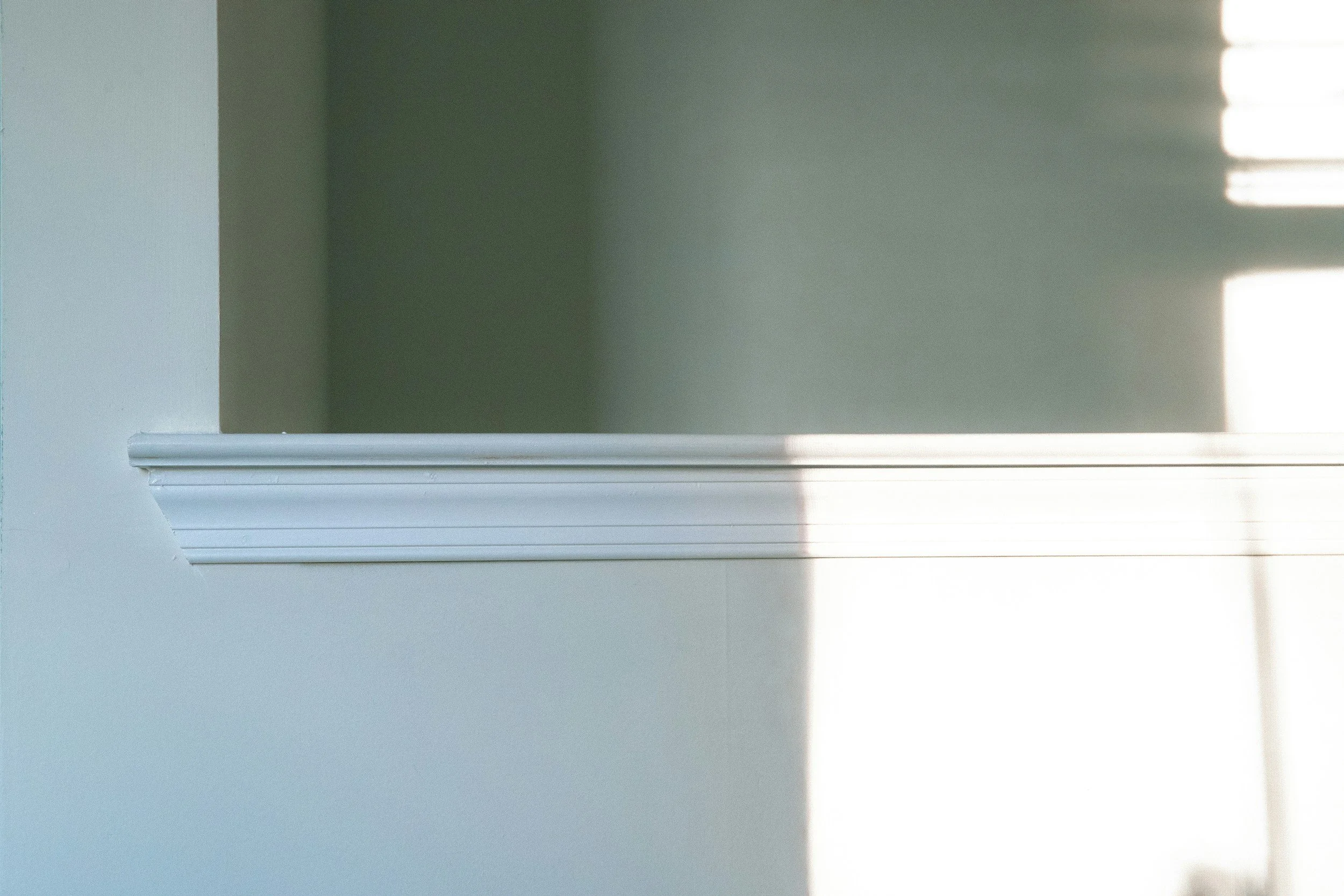 A white painted wall with a white crown molding at the bottom, divided into two sections with shadowed and lit areas.