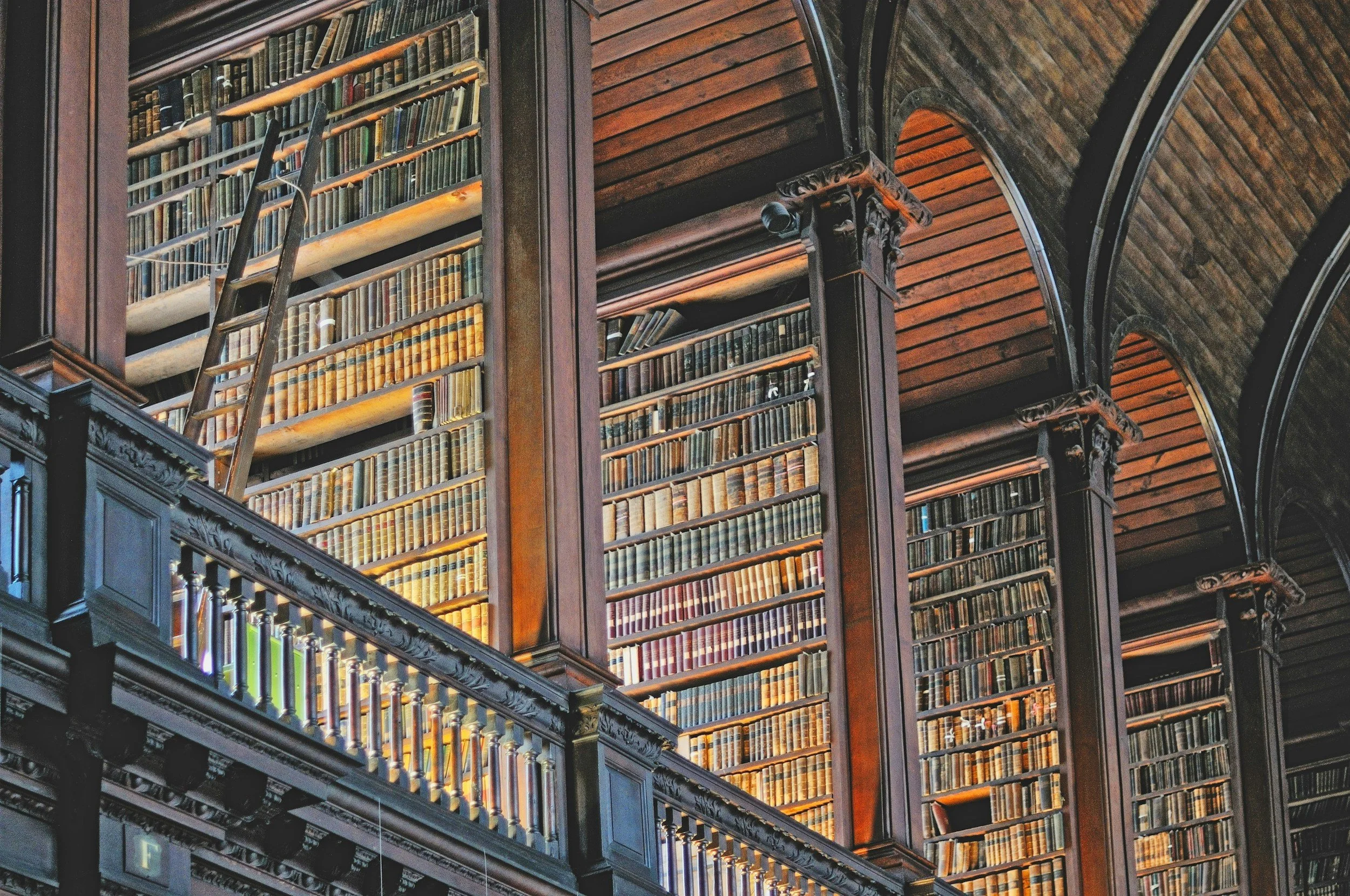Interior view of a historic library with tall bookshelves filled with old books, intricate woodwork, and arched ceilings.