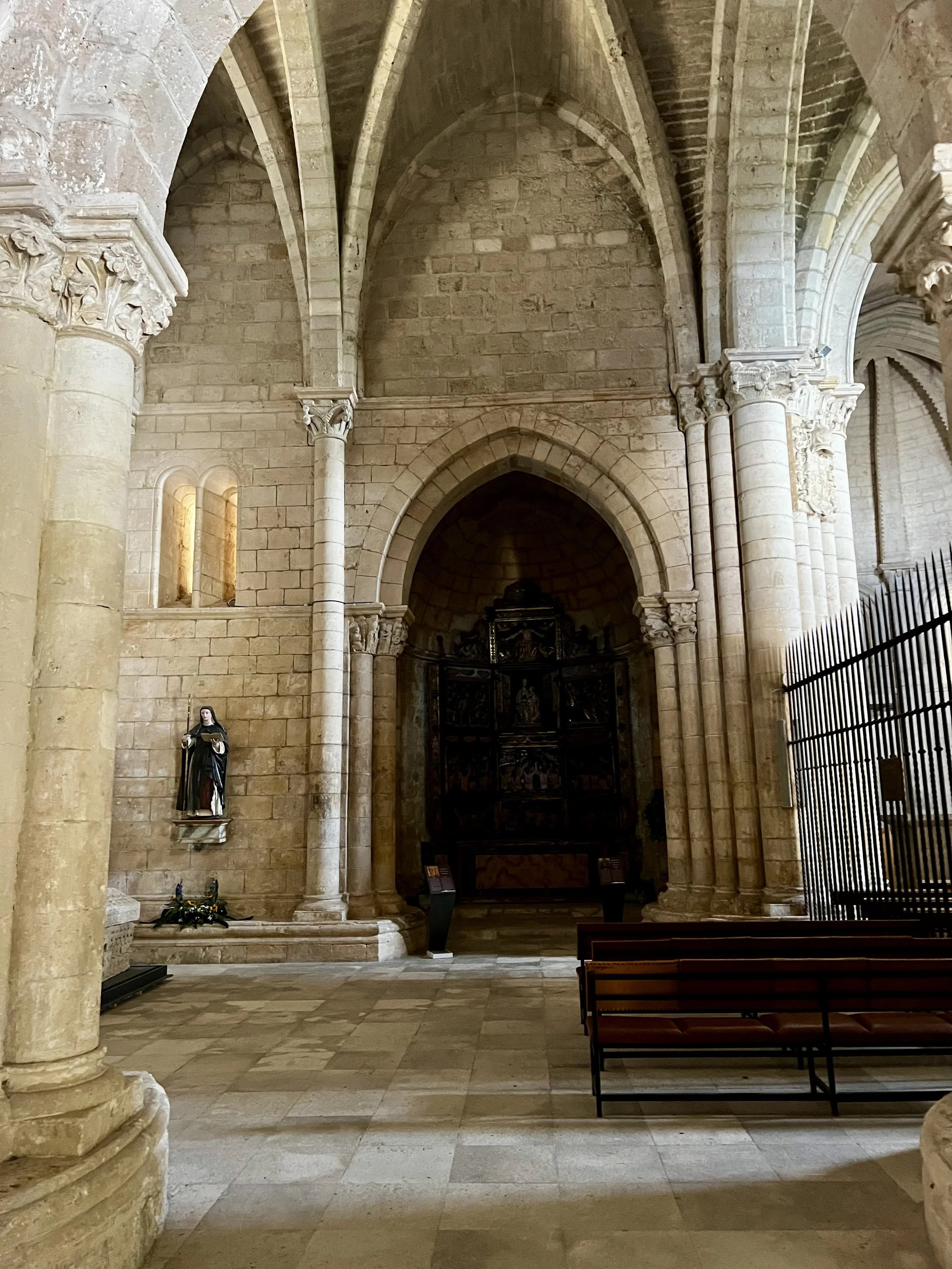 Interior of a historic stone church with columns, statues, wooden benches, and religious artwork.