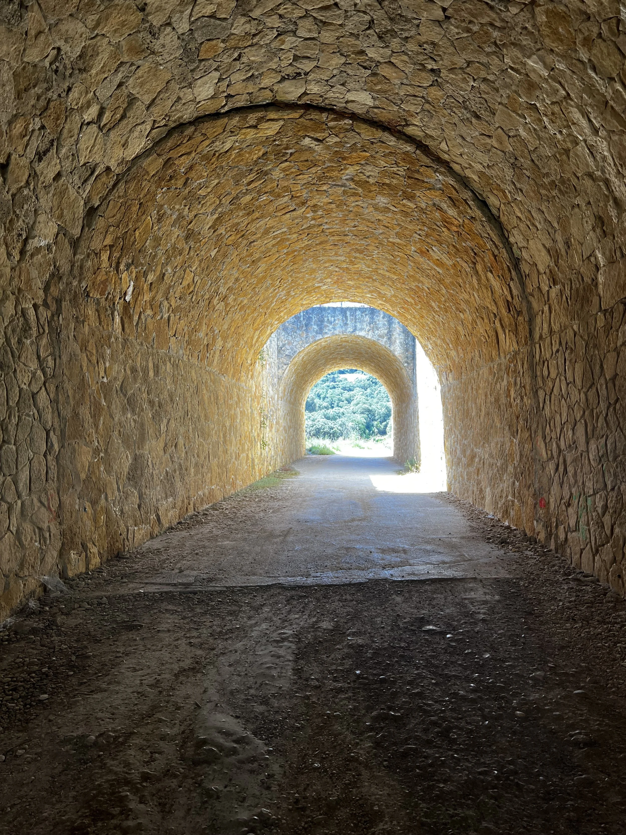 A stone tunnel with arched ceiling and a bright opening at the end showing outdoor greenery