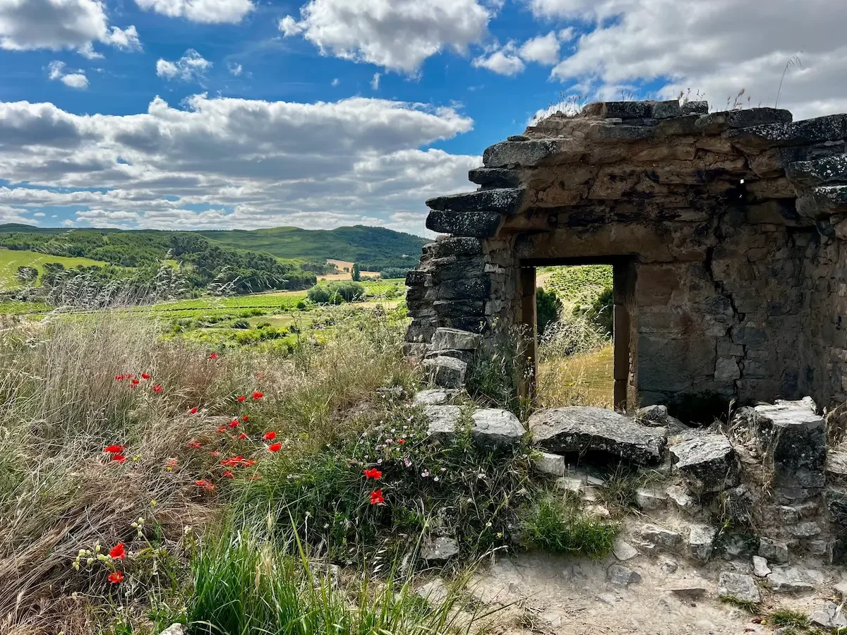 Ruins of an old stone building overlooking a green landscape with rolling hills and a partly cloudy sky.