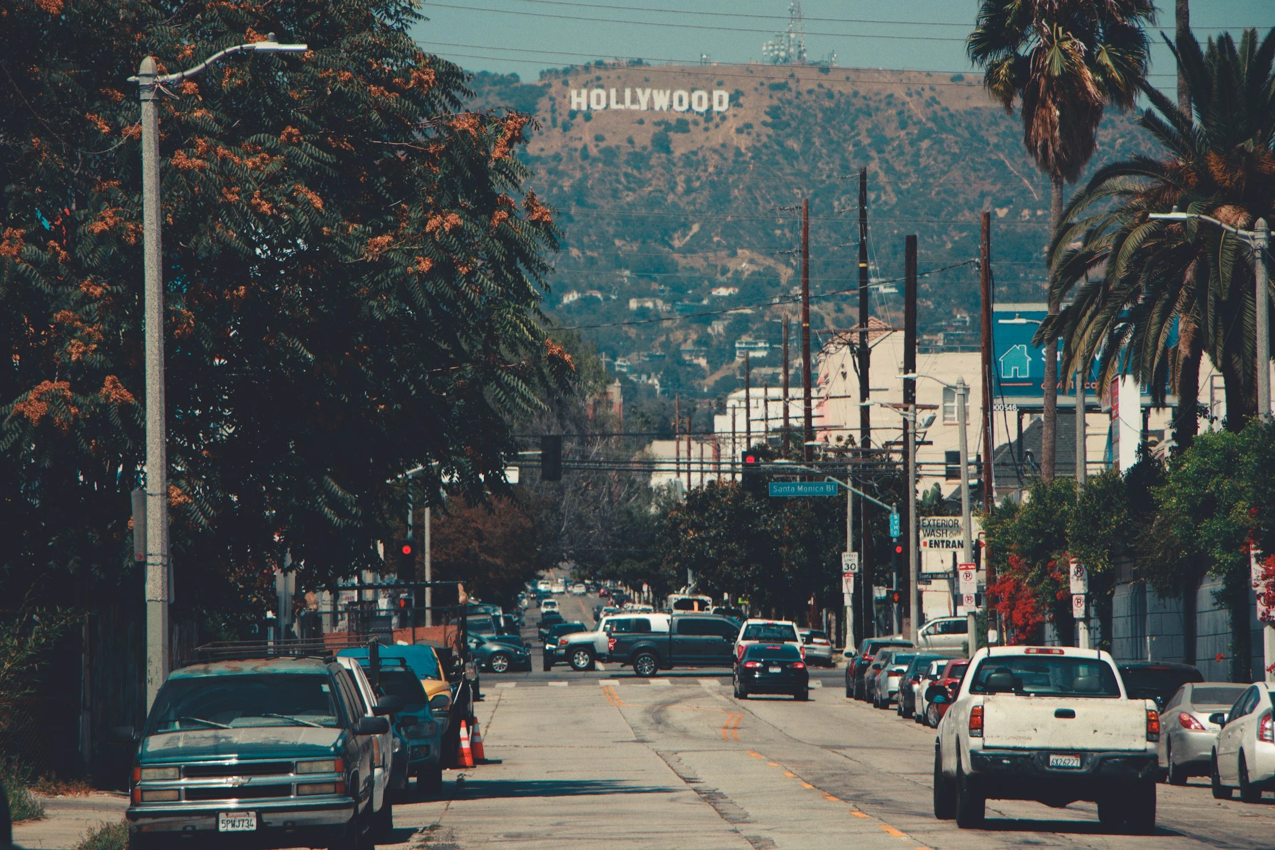 Street scene in Hollywood with cars parked along the road and the Hollywood sign on the hillside in the background.