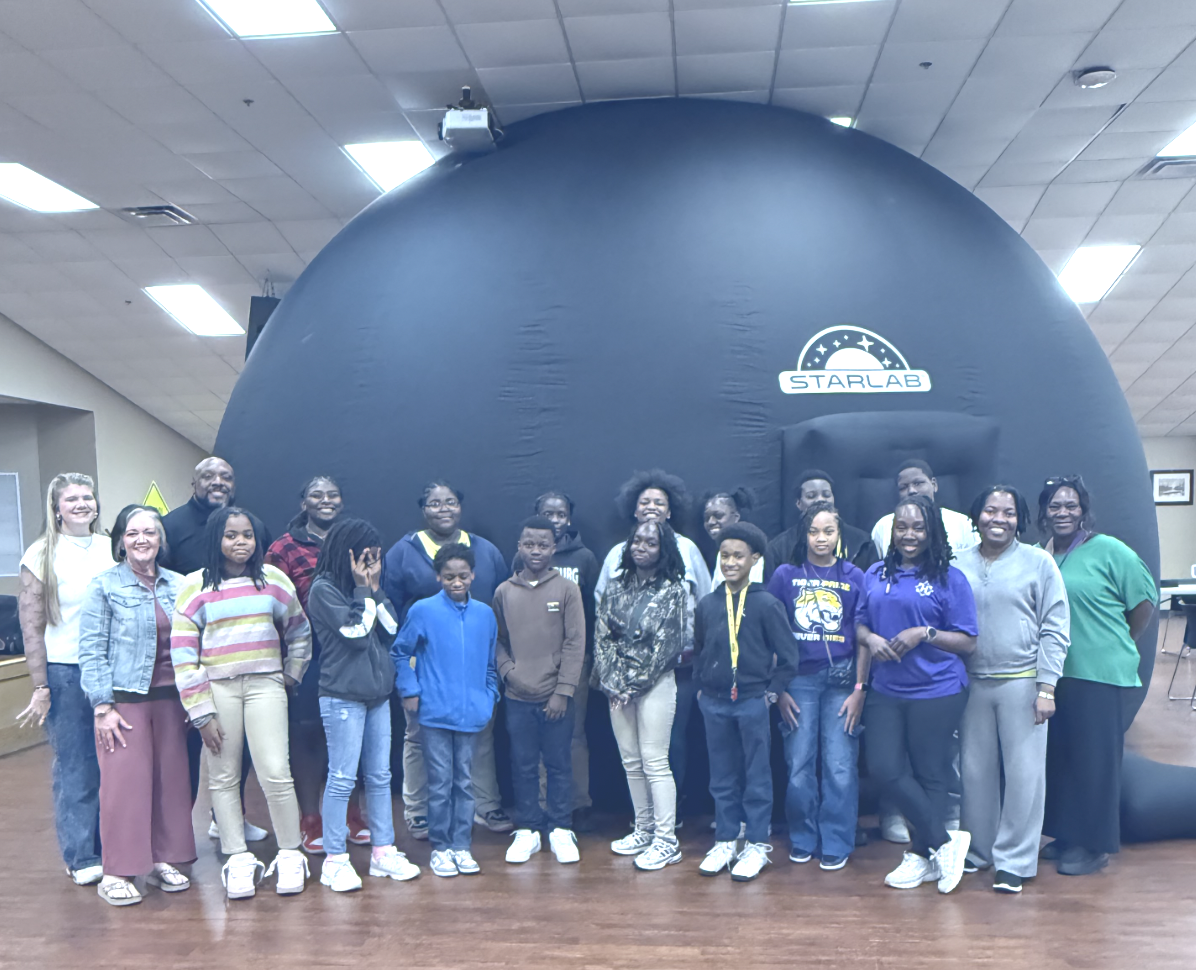 Group of children and adults standing in front of a large black inflatable structure with a 'STARLAB' logo indoor facility.