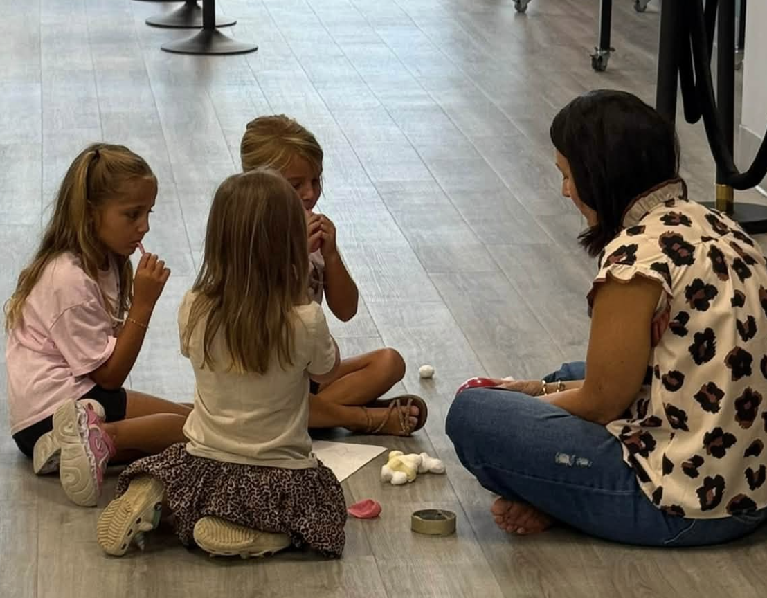 Four children sitting on the floor in a circle with a woman, appearing to be engaging in a group activity.