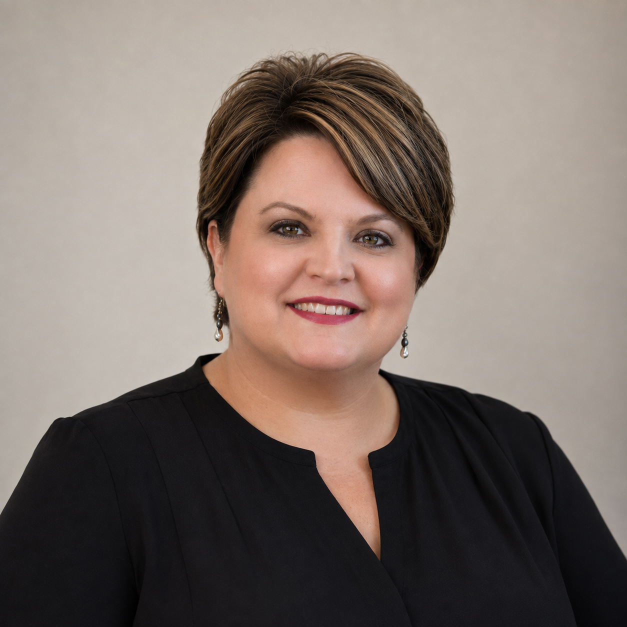 Professional woman with short brown hair and earrings, wearing a black top, smiling against a neutral background.